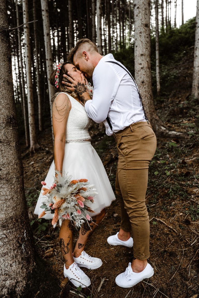 Couple tatoue qui s'embrassent dans les bois lors de leur mariage